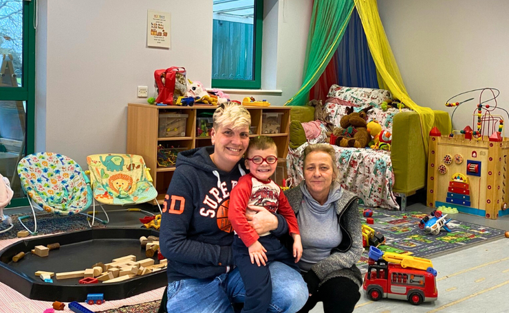 Two women kneeling on the floor with their son in the middle at a family centre with toys in the background
