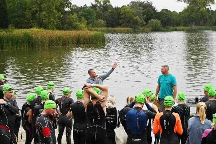 Multiple swimmers in green caps getting instructions by body of water
