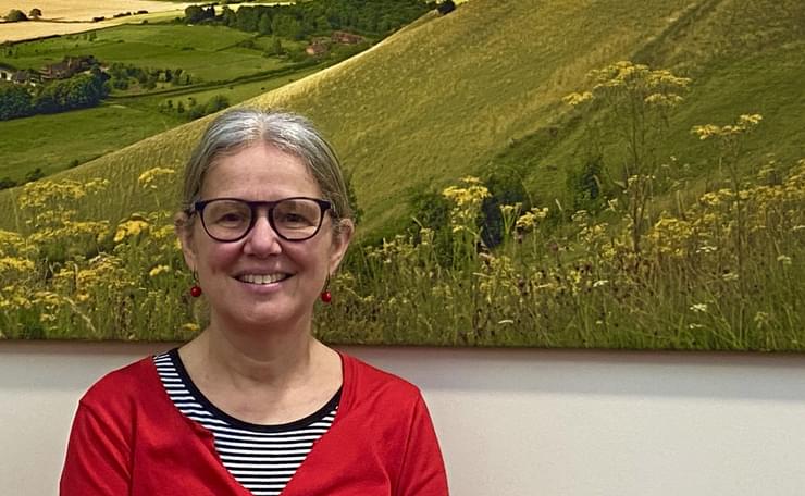 Photograph of Katie Glover, CEO of West Sussex Mind, in front of large photograph of the countryside