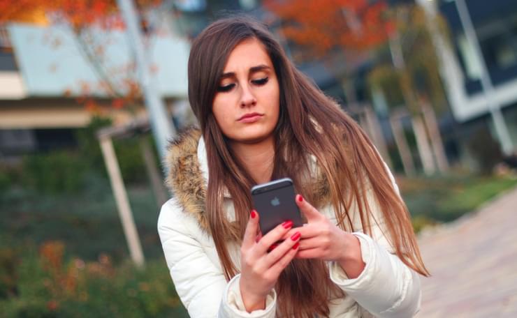 Woman, looking serious, with her mobile phone outside