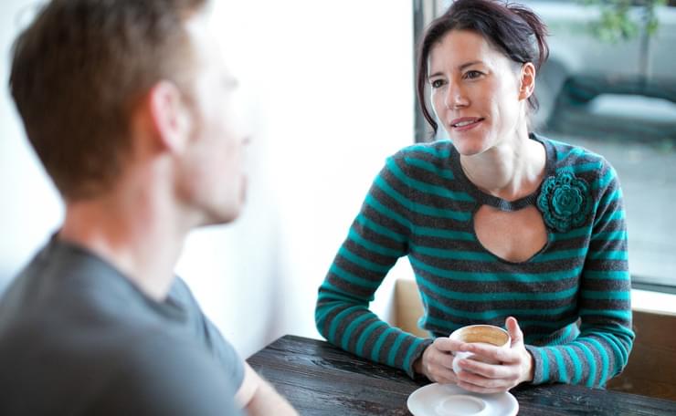 Woman listening to man over cup of coffee