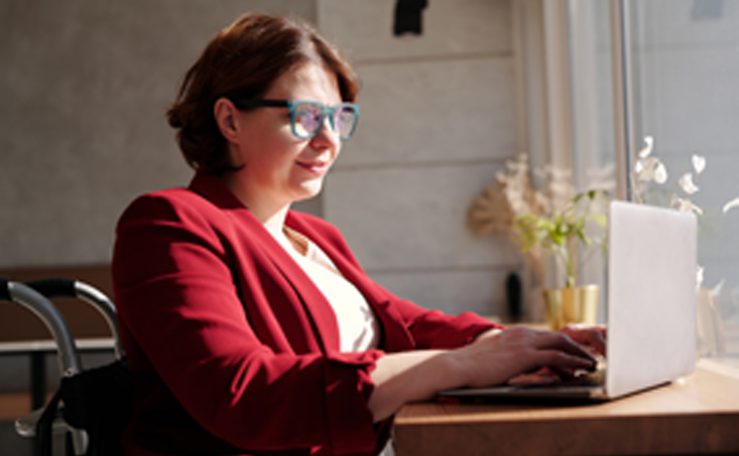Woman in red jacket on laptop with wheelchair just visible