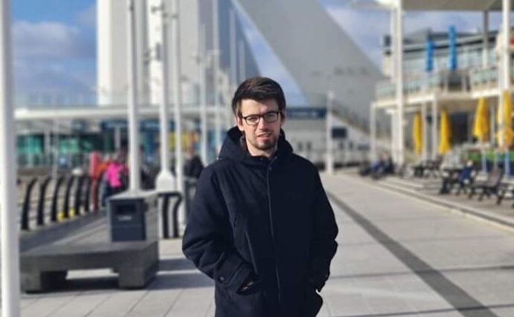 Young man standing on the waterfront wearing jeans, trainers and a warm coat