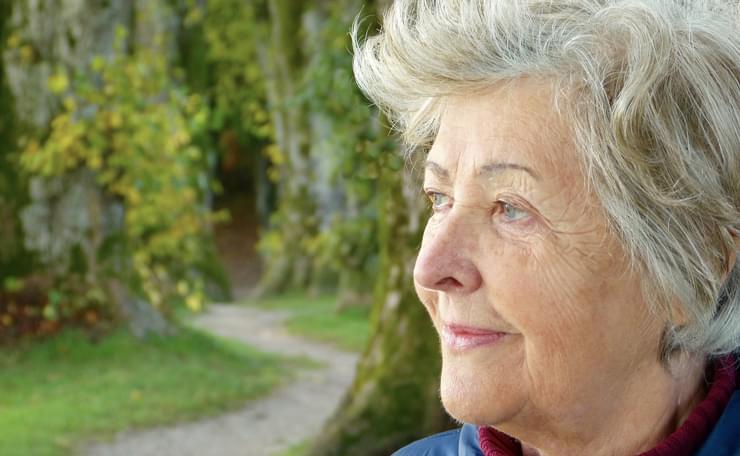 Older woman looks to the side with greenery behind