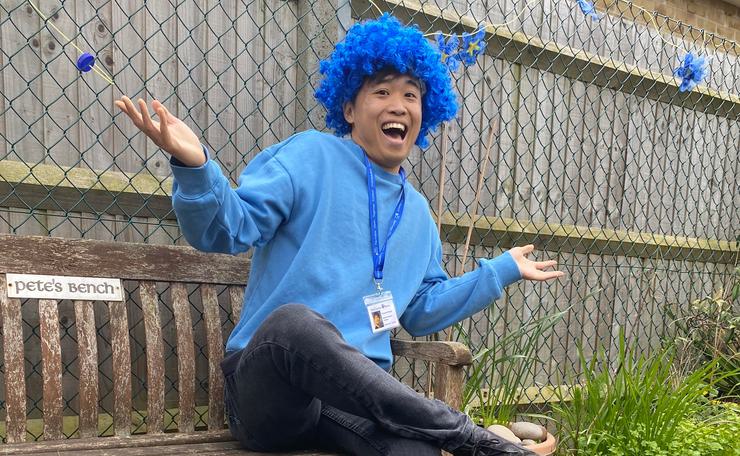 Man sitting on a bench in a blue wig and jumper