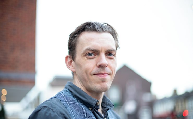 Photo of man in his late twenties early thirties smiling to camera against a blurred background