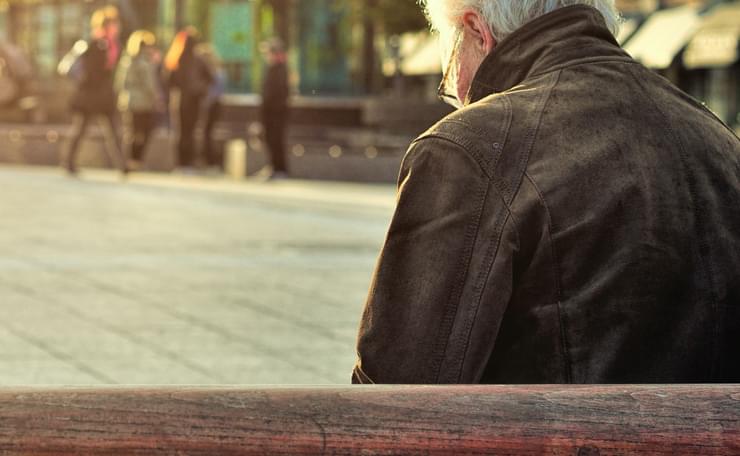 Older man sitting on a bench with his back to the camera